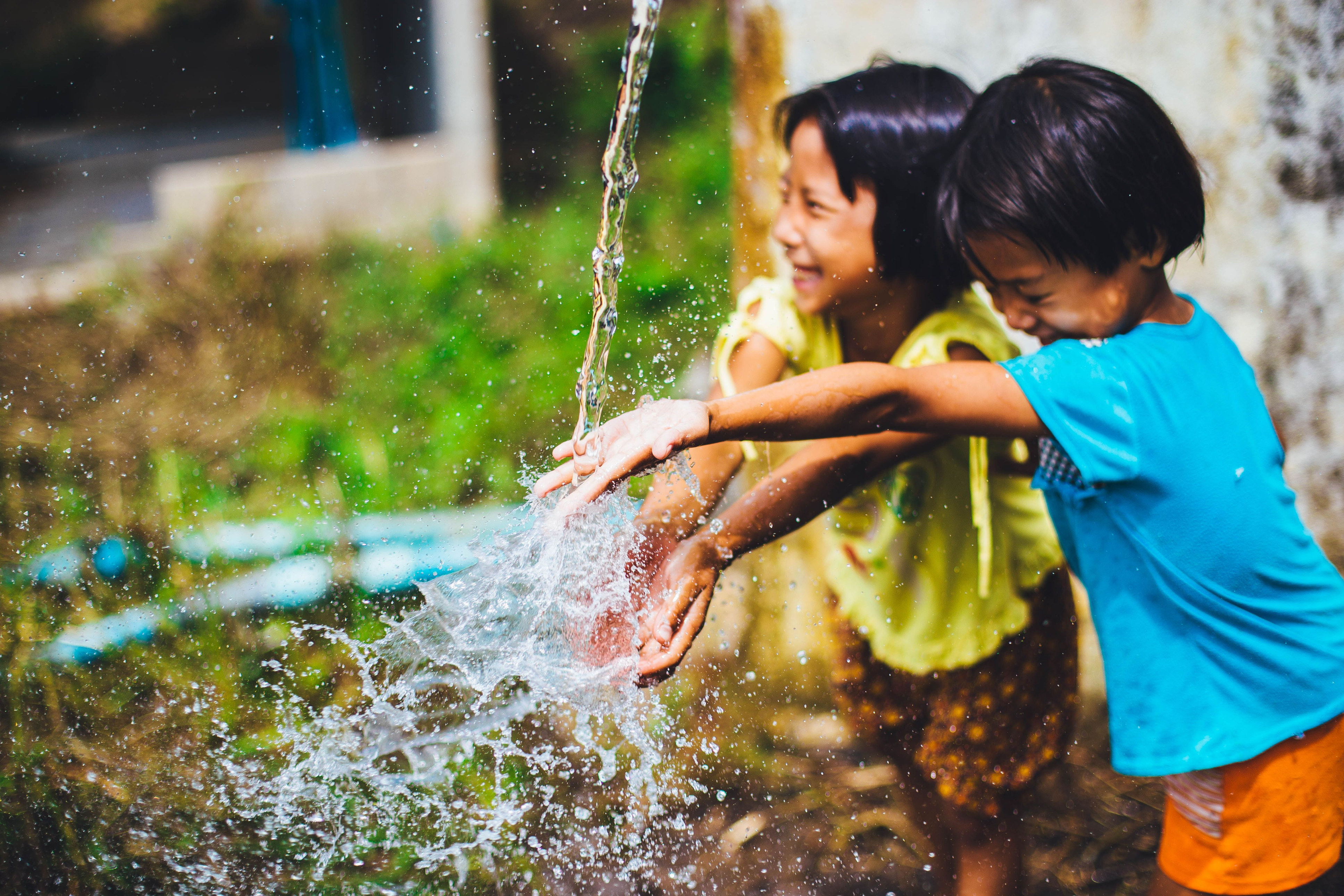 two kids smiling while they wash their hands